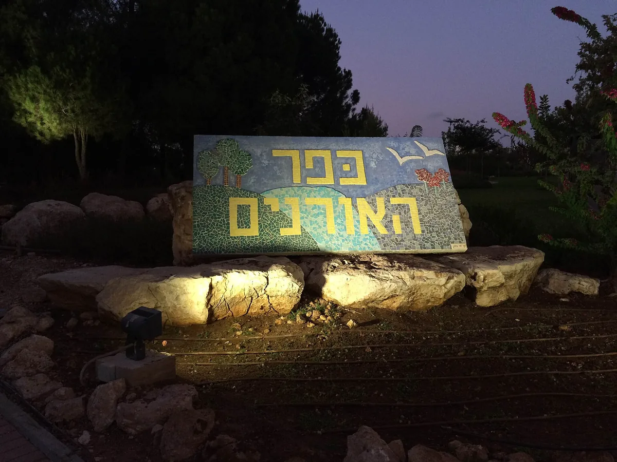 The lit mosaic sign at the entrance to Kfar HaOranim at dusk