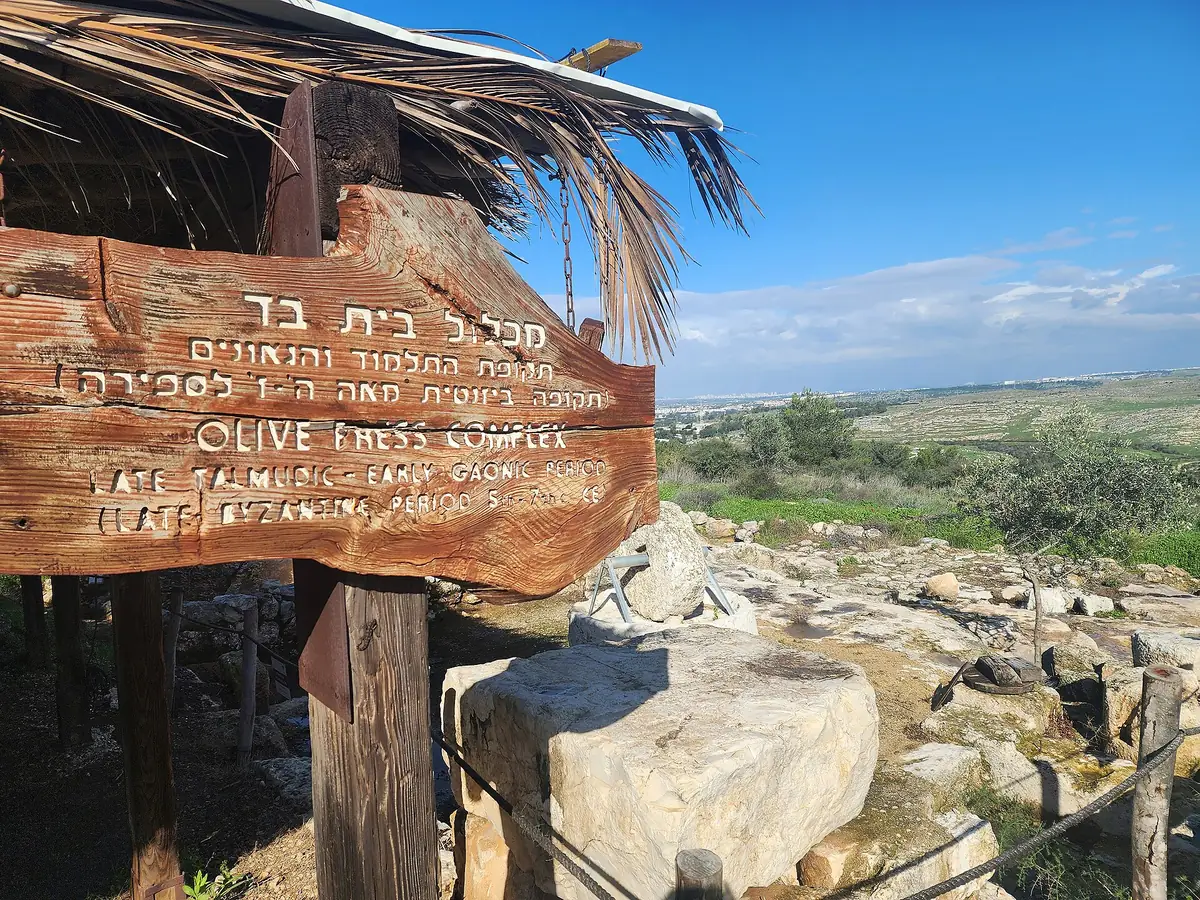 A wooden sign for the olive press complex at Neot Kedumim beside ancient stone remains